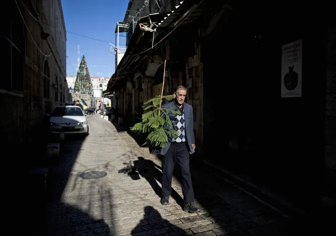Un Palestinien portant un sapin de Noël dans une rue pavée de la vieille-ville de Jérusalem. Keystone/ Abir Sultan